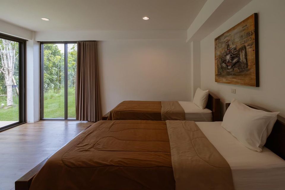 Bedroom with two twin beds, brown bedding, and large windows overlooking a lush garden at The Valley Khaoyai V Villa.