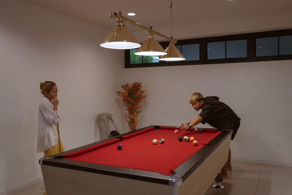 Guests enjoy a game of billiards on the red felt pool table in the entertainment room at The Valley Khaoyai V Villa.