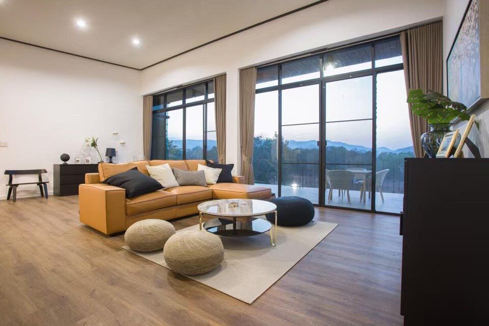 Spacious living room with a tan sectional sofa, round coffee table, and large windows overlooking mountains at The Valley Khaoyai V Villa.