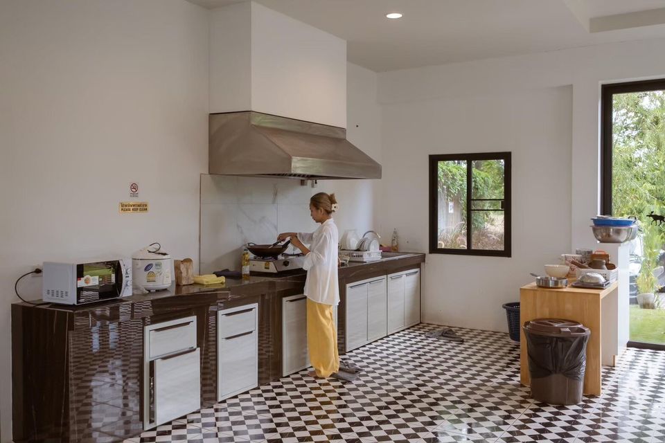 A guest cooks in the spacious, well-equipped kitchen of The Valley Khaoyai V Villa, featuring a stove, microwave, and checkered floor.