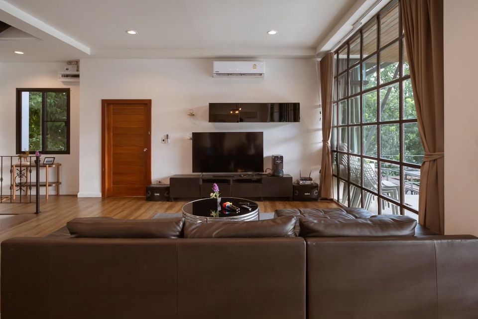 Spacious living room at The Valley Khaoyai V Villa with a large brown sofa, TV, and floor-to-ceiling windows.