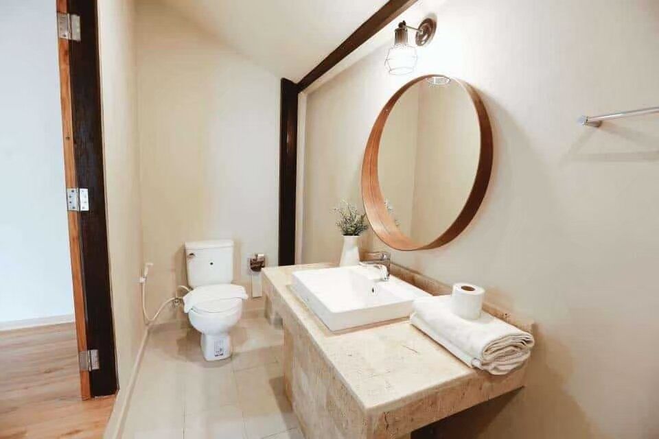 Modern bathroom with a round wooden mirror, white vessel sink, and toilet at The Valley Khaoyai I, Khao Yai.