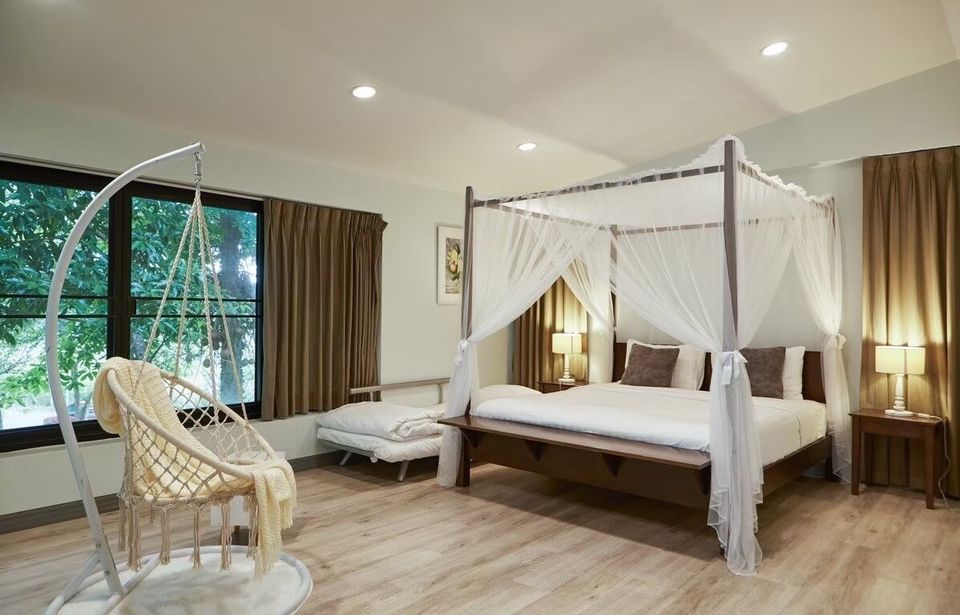 A cozy bedroom at The Valley Khaoyai I in Khao Yai, featuring a romantic canopy bed and a hanging swing chair by the window.