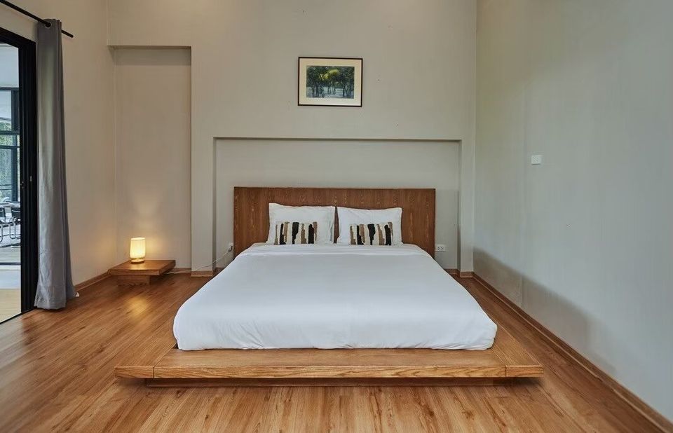 Minimalist platform bed with white linens and wooden headboard in a bedroom at The Valley Khaoyai I, Thailand.