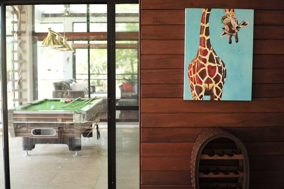 A pool table with cues and balls visible through glass doors at The Valley Khaoyai I, with a giraffe painting on a wooden...