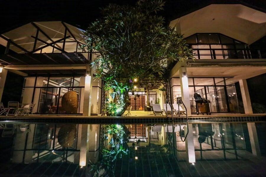 The Valley Khaoyai I pool villa at night, showcasing the illuminated exterior and its reflection in the dark pool water.