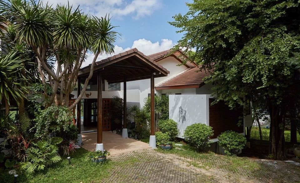 The Valley Khaoyai I villa entrance with covered walkway, lush tropical plants, and a paved driveway under a blue sky.