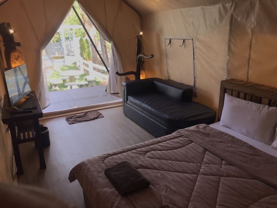 Cozy glamping tent bedroom at The Valley Khaoyai IX Villa, Khao Yai, featuring a comfortable bed, sofa, and TV, with an outdoor view.