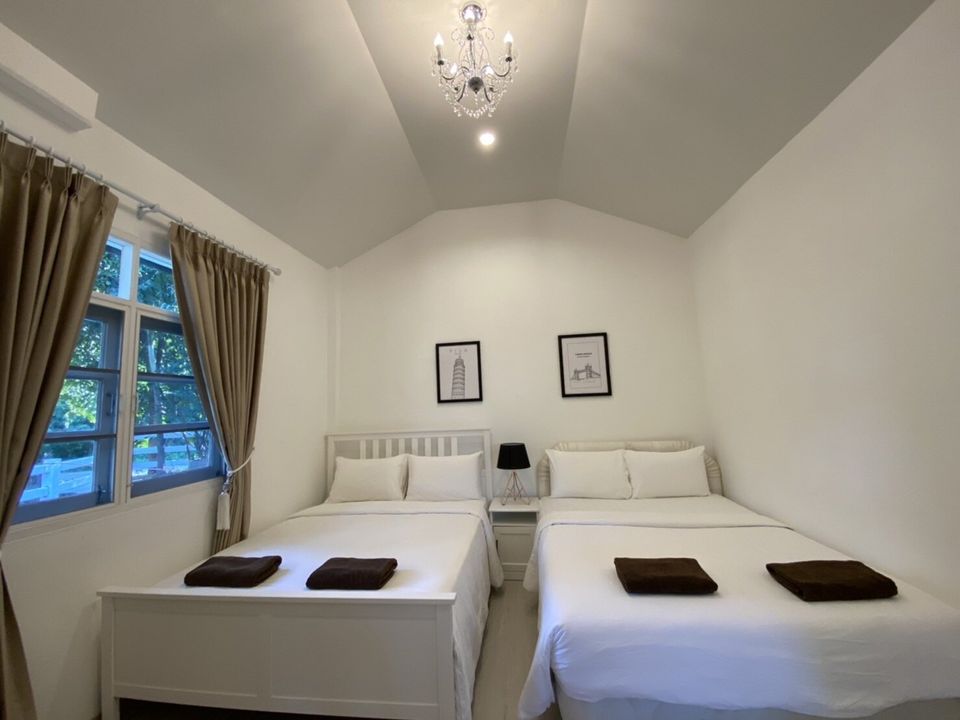 Bright bedroom at The Valley Khaoyai IX Villa with two double beds, white linens, and a stylish chandelier. Perfect for families.
