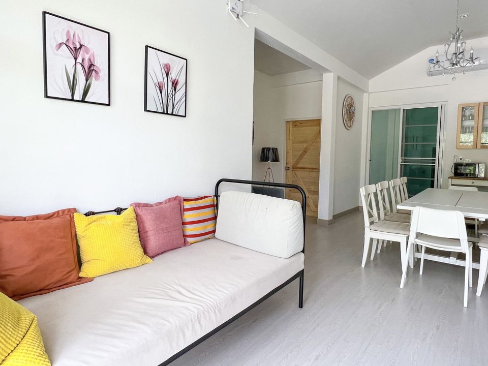 Bright living area at The Valley Khaoyai IX Villa with a sofa, colorful cushions, and a dining table in the background.