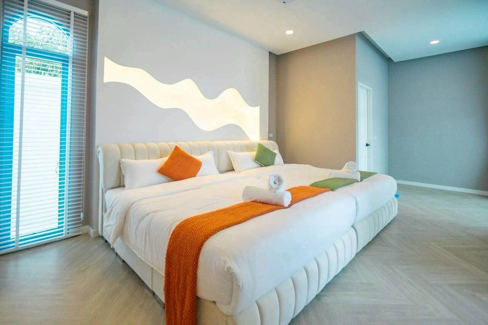 A spacious bedroom at Tierra V Pool Villa, Pattaya, featuring a king-size bed with orange and green accents and unique wall lighting.