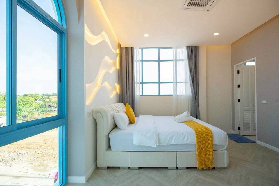 Bright bedroom at Tierra V Pool Villa, Pattaya, featuring a comfortable king-size bed with yellow accents and unique wall lighting.