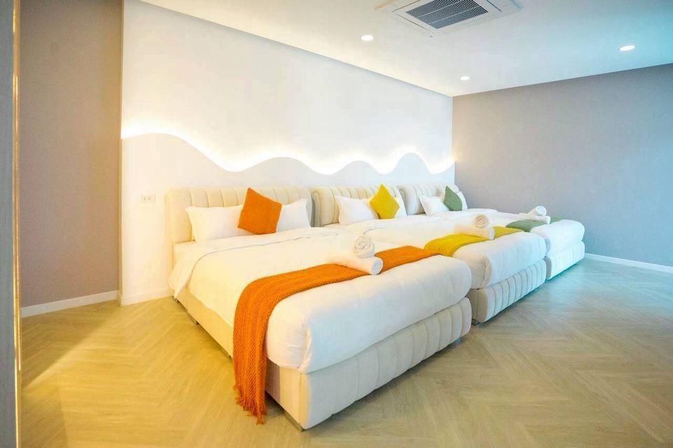 Bright bedroom at Tierra V Pool Villa, Pattaya, featuring two king-sized beds with colorful throws and pillows, and unique wave-patterned wall lighting.