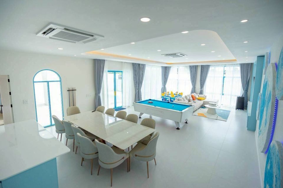 Spacious open-plan living area at Tierra V Pool Villa, Pattaya, featuring a large dining table and a vibrant blue pool table.