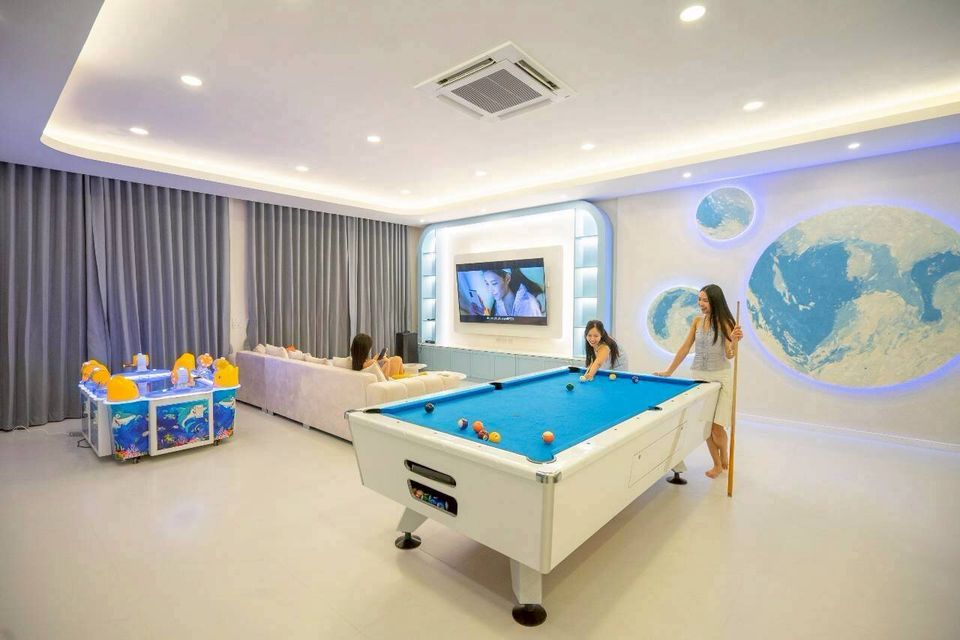 Guests enjoy billiards and arcade games in the entertainment room at Tierra V Pool Villa, Pattaya. Features a large TV.