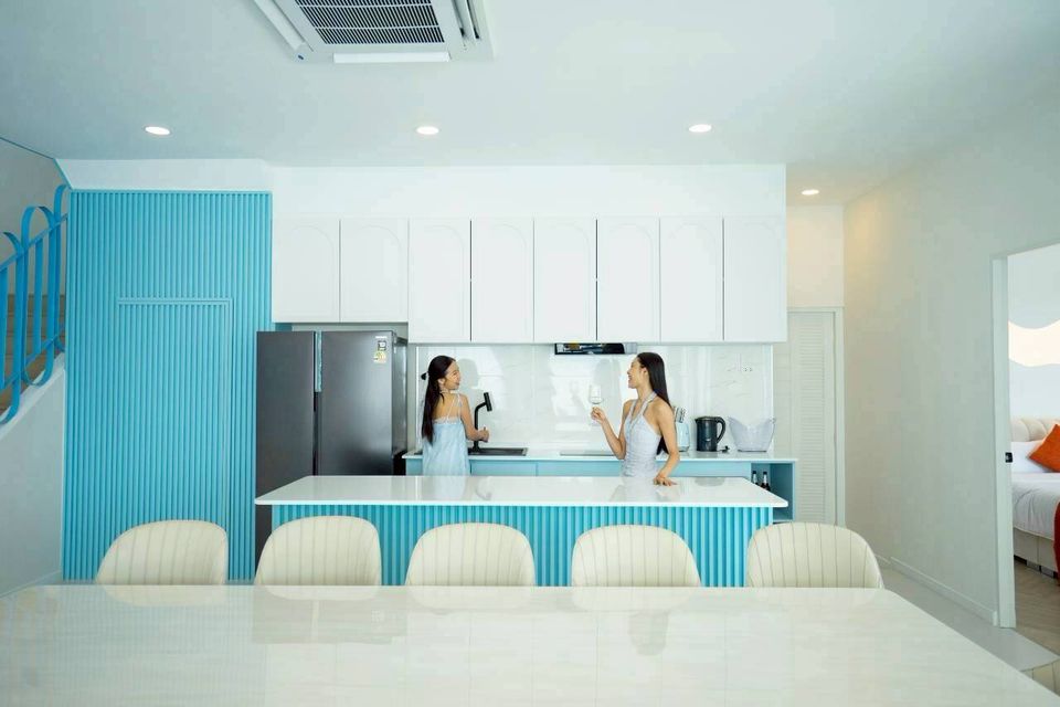Two women in the bright, modern kitchen of Tierra V Pool Villa Pattaya, featuring blue accents and a large island.