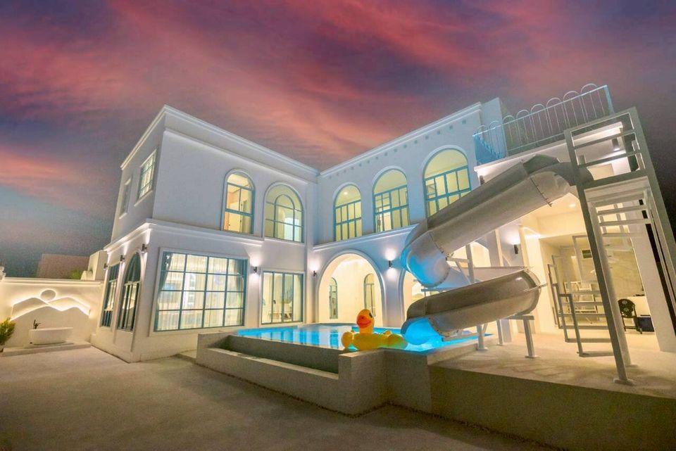 Tierra V Pool Villa Pattaya at dusk, showcasing the illuminated pool with a fun water slide and a large yellow duck float.