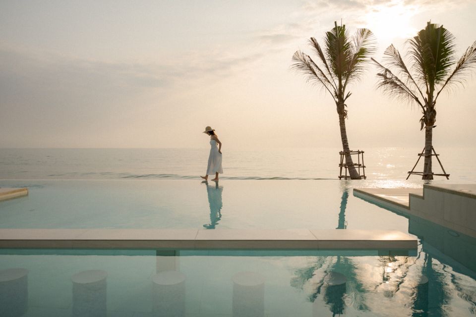 Woman walks along the infinity edge pool at Valika VIII Pool Villa, Hua Hin, with ocean view and palm trees.