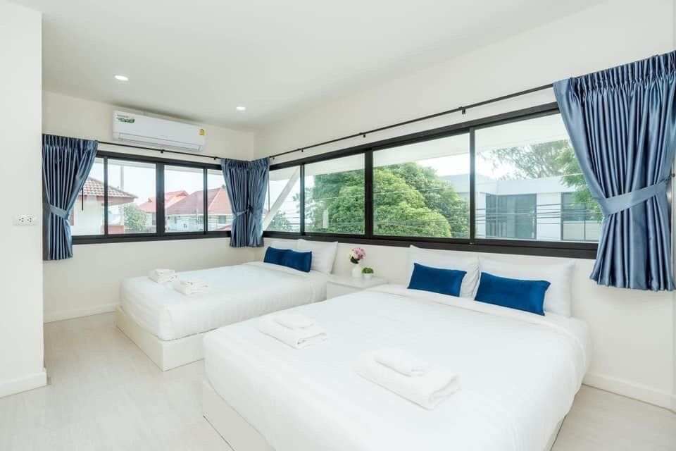 Bright bedroom at View Lay IV Pool Villa, Cha-Am, featuring one double bed and one twin bed with blue pillows and large windows.