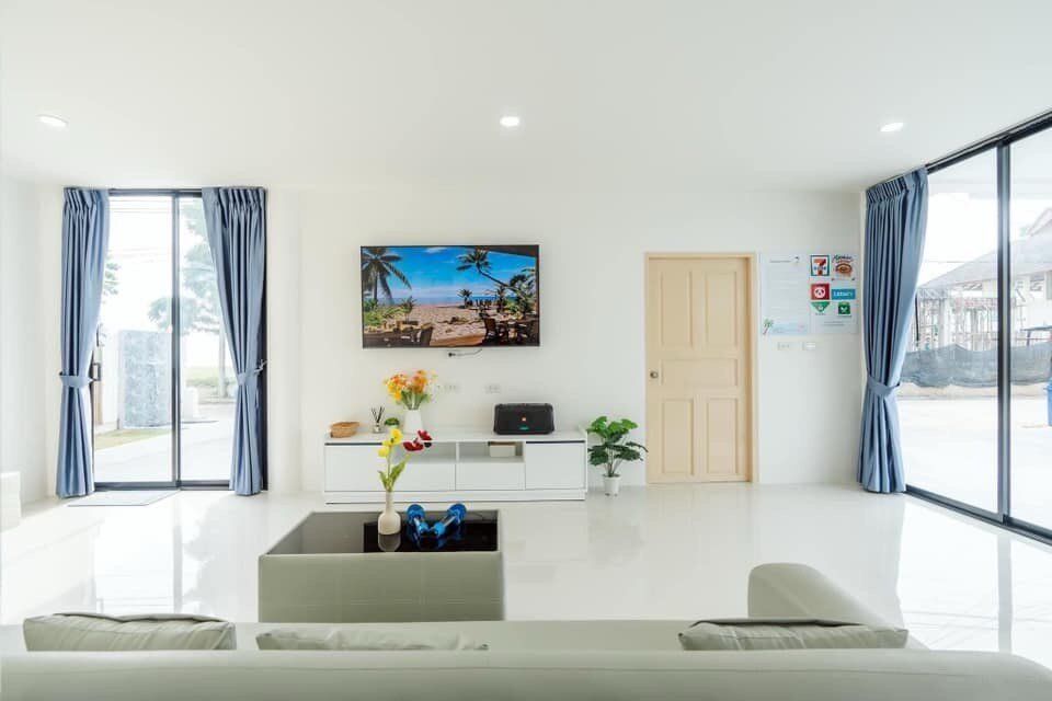 Bright, modern living room at View Lay IV Pool Villa, Cha-Am, featuring a large TV, white sofa, and sliding glass doors.