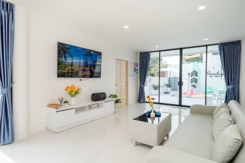 Bright living room at View Lay IV Pool Villa, Cha-Am, with a large TV, white sofa, and sliding doors to the pool.