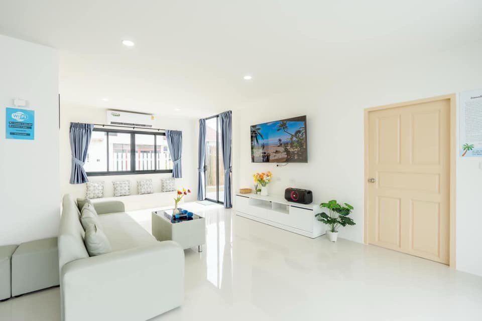 Bright living room at View Lay IV Pool Villa, Cha-Am, with white sofa, wall-mounted TV, and large windows.