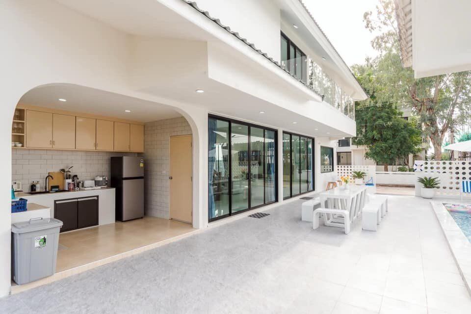 Outdoor dining area with white table and benches next to an open-air kitchen at View Lay IV Pool Villa, Cha-Am.