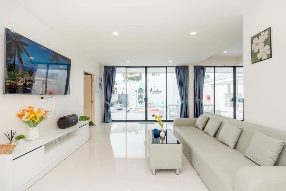 Bright living room at View Lay IV Pool Villa, Cha-Am, with a large TV, comfortable sofa, and glass doors opening to the pool.