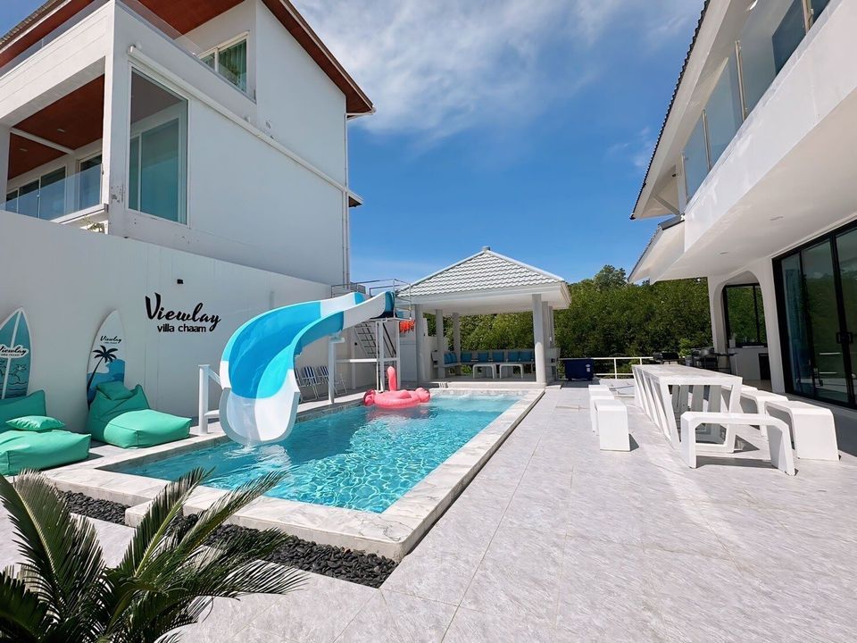 View Lay IV Pool Villa in Cha-Am features a refreshing outdoor pool with a fun blue and white water slide and a pink flamingo float.
