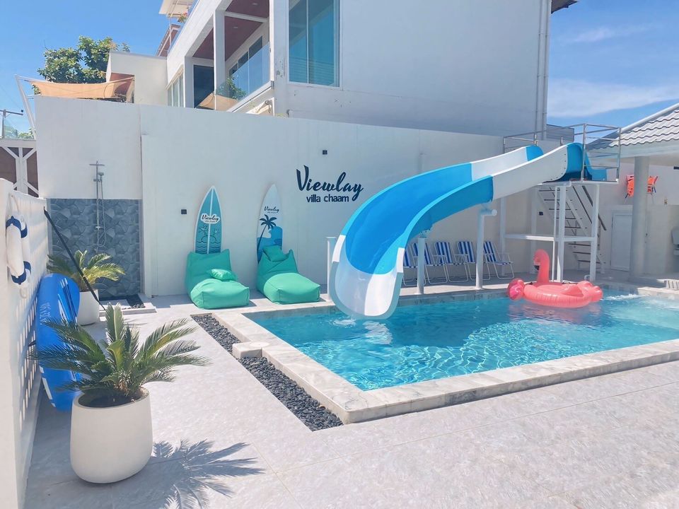 Bright outdoor pool area at View Lay IV Pool Villa, Cha-Am, featuring a blue and white water slide and a pink flamingo float.